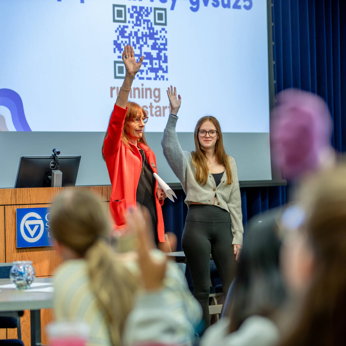 A student and a staff member stand at the front of a room with their right hands raised